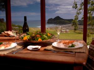 a table with a plate of food and a salad at Bethells Beach Cottages in Bethells Beach