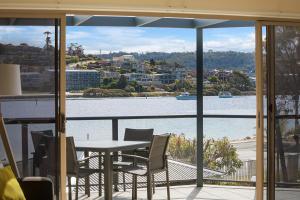 balcón con mesa, sillas y vistas al río en Sails Luxury Apartments Merimbula, en Merimbula