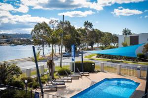 a swimming pool with lounge chairs next to a body of water at Sails Luxury Apartments Merimbula in Merimbula