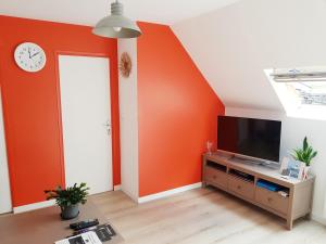 a living room with an orange accent wall and a tv at Gite de Beg Menez Le 14 - Gite à la Forêt Fouesnant in La Forêt-Fouesnant