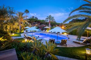 a pool at night with umbrellas and palm trees at Vila Balaia - Luxury Boutique Villas in Albufeira
