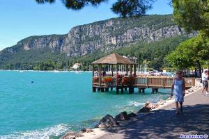 a woman walking on a beach with a gazebo on the water at GardaGulf EdenGarden in Garda