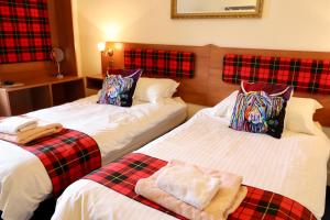 two beds in a hotel room with plaid pillows at Highland House Callander in Callander