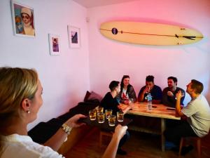 een groep mensen die rond een tafel zitten met een surfplank aan de muur bij Jimmy Jumps House in Vilnius