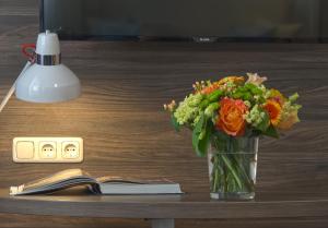 a vase of flowers on a table next to an alarm clock at Lizz Hotel Munich in Munich