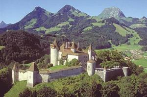 un castillo en una colina con montañas en el fondo en Charmant Petit Chalet 3 étoiles en Gruyère en Crésuz