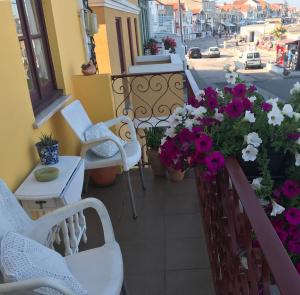 a balcony with white chairs and flowers on a street at Pensão José das Hortas in Costa Nova