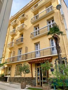 a yellow building with balconies and a palm tree in front of it at Hôtel des Bains et des Gorges in Amélie-les-Bains-Palalda