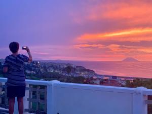 une femme prenant une photo du coucher du soleil depuis un balcon dans l'établissement Villino Eleonora, à Parghelia