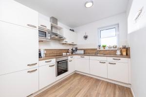 a kitchen with white cabinets and a wooden floor at Sommer Kajüte in Olpenitz
