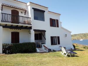 a white house with a balcony and a chair at Casa con jardin ,vistas al mar y atardecer en Playas de Fornells in Es Mercadal