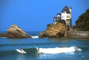 zwei Menschen reiten Wellen auf Surfbrettern im Ozean mit einem Schloss in der Unterkunft Petit appartement douillet très bien situé in Biarritz