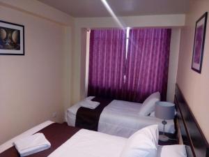 2 camas en una habitación de hotel con cortinas moradas en BLUEIBY HOME, en Cusco