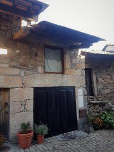 una casa de piedra con una puerta negra y una ventana en Abrigo Montesinho, en Montezinho