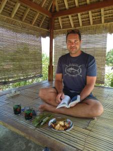 a man sitting on a table with a plate of food at Crispycool Homestay in Kuta Lombok
