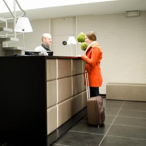 una mujer con una maleta parada en un mostrador con un hombre en Hotel Essenza, en Puurs