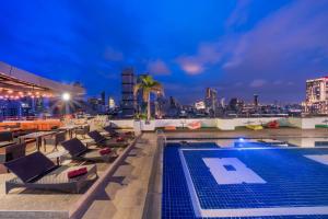 een zwembad op het dak met stoelen en een skyline van de stad bij Furama Silom Hotel in Bangkok