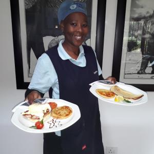 a woman is holding two plates of food at Bayside Lodge in Plettenberg Bay