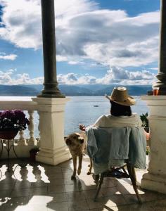 eine Person, die auf einem Stuhl sitzt, mit einem Hund, der auf das Wasser schaut in der Unterkunft Town House Messina Paradiso in Messina