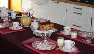 una mesa con platos y tazas y un tazón de comida en Le Clos du Jubin, en Saint-Forgeux