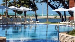 a swimming pool with white chairs and umbrellas at Jatiuca Hotel & Resort in Maceió