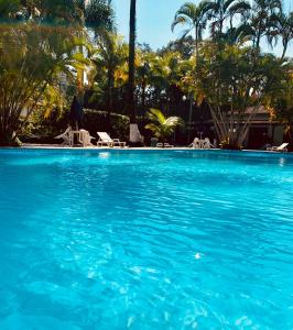 une grande piscine bleue avec des chaises et des palmiers dans l'établissement Boiçucanga Completo à Beira Mar, à Boicucanga