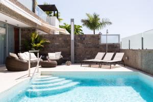 a swimming pool with two chairs and a table next to a house at Luxury BKM in Playa del Duque in Adeje