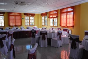 un salón de banquetes con mesas y sillas blancas y ventanas en Hotel Meleiros, en Castro de Sanabria