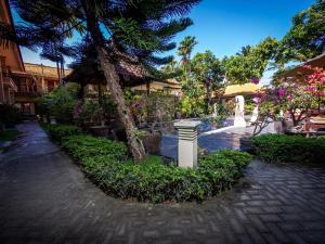 un patio con un árbol y flores y una fuente en Yulia Beach Inn Kuta, en Kuta