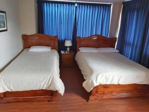 2 camas en un dormitorio con cortinas azules en Hostal Tutamanda 2, en Quito