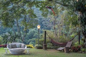 a hammock in a garden with a chair and a lamp at Pousada Quinta dos Pássaros Itaipava in Itaipava