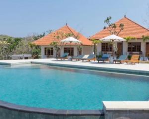 a pool with chairs and umbrellas next to a house at Batu Jaran Hill Cottage Uluwatu in Uluwatu
