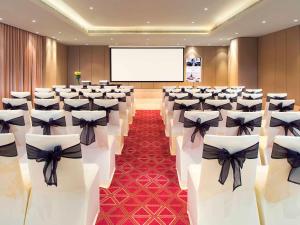 Mercure Hyderabad KCP Banjara Hills, An Accor Hotel في حيدر أباد: قاعة اجتماعات مع كراسي بيضاء مع بعرصي سوداء