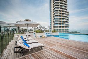 een terras met ligstoelen en een parasol naast een zwembad bij The Capital Pearls Hotel in Durban