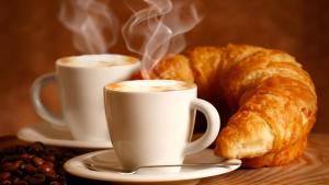 two cups of coffee and a croissant on a table at NEW Bcomfort in Cagliari