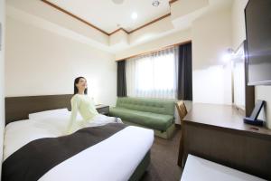 a woman sitting on a bed in a hotel room at Maple Inn Makuhari in Chiba