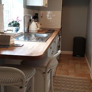 a kitchen with a sink and a counter with two chairs at The Nest at Bramble Cottage Lacock in Lacock