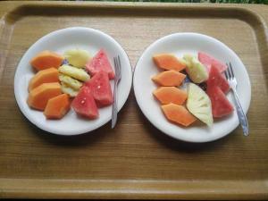 two plates of fruit on a tray with forks and knives at Purnama di Bisma in Ubud