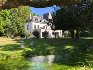 a house with two chairs in front of a river at Chaumière au bord de l'eau - Domaine de 3 hectares - Borne Electrique - Chiens acceptés in Hondouville
