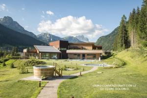a building in a field with mountains in the background at Hotel Nès Crépes in Pozza di Fassa