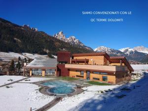a building in the snow with mountains in the background at Hotel Nès Crépes in Pozza di Fassa
