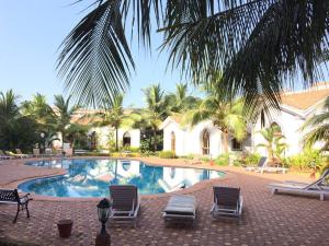 a swimming pool with chairs and palm trees and a house at Casa Legend Villa & Apartments Arpora - Baga - Goa in Baga
