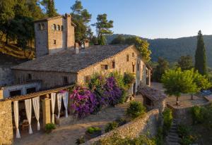 an old stone building with purple flowers and a tower at Masia Can Pou in Canet de Adri