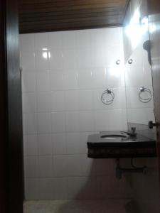 a white tiled bathroom with a sink and a mirror at Centerminas Palace Hotel in Curvelo