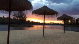 3 sombrillas de paja en una playa con un lago en Palacete Dos Alcaides, en Minas de São Domingos