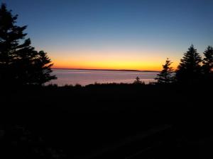 a sunset over the water with trees in the foreground at Private Waterfront Luxury on the Bras D'Or Lake in Sydney Forks