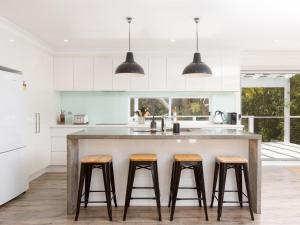 a kitchen with white cabinets and a large island with bar stools at Amalfi Beach House in Gerringong