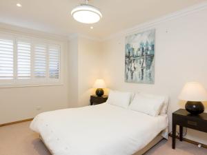 a white bedroom with a white bed and two lamps at Coastal Haven at Gerroa in Gerroa