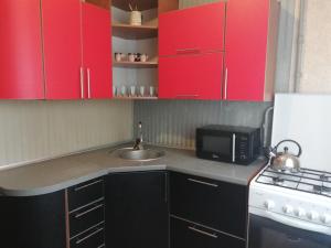 a kitchen with red cabinets and a sink and a microwave at Заслонова 24 центр города in Salihorsk