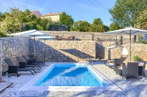 a swimming pool with chairs and umbrellas next to a stone wall at Villa Vrh in Krk